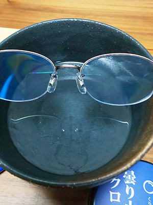黒い器の上に眼鏡。右側は細かい水滴、左側は油膜のようなものが見える。