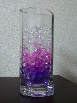 ガラス製の花瓶に入ったウォータービーズがパープル、ピンク、クリアのグラデーションになっている。